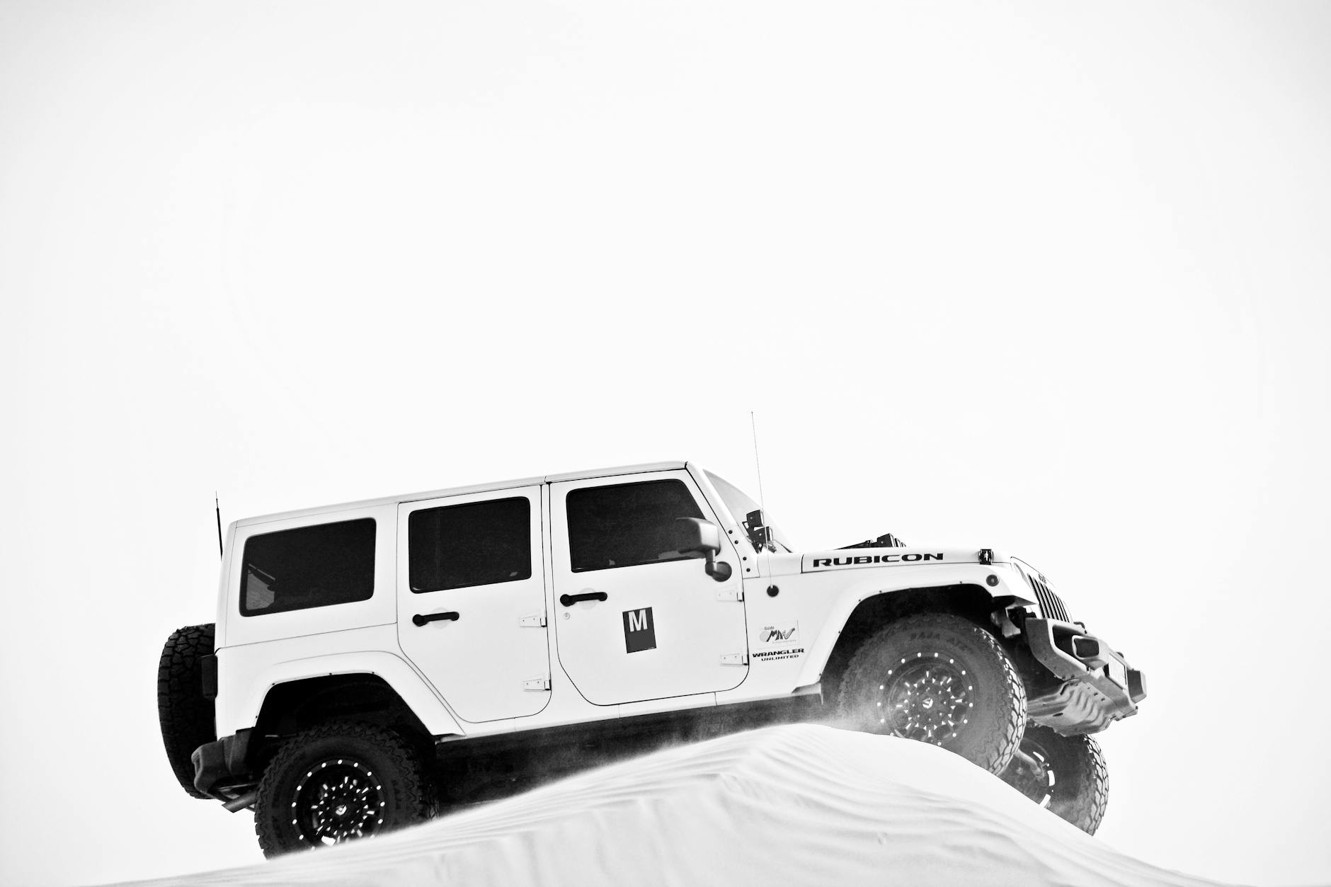 grayscale photo of white jeep on sand dune