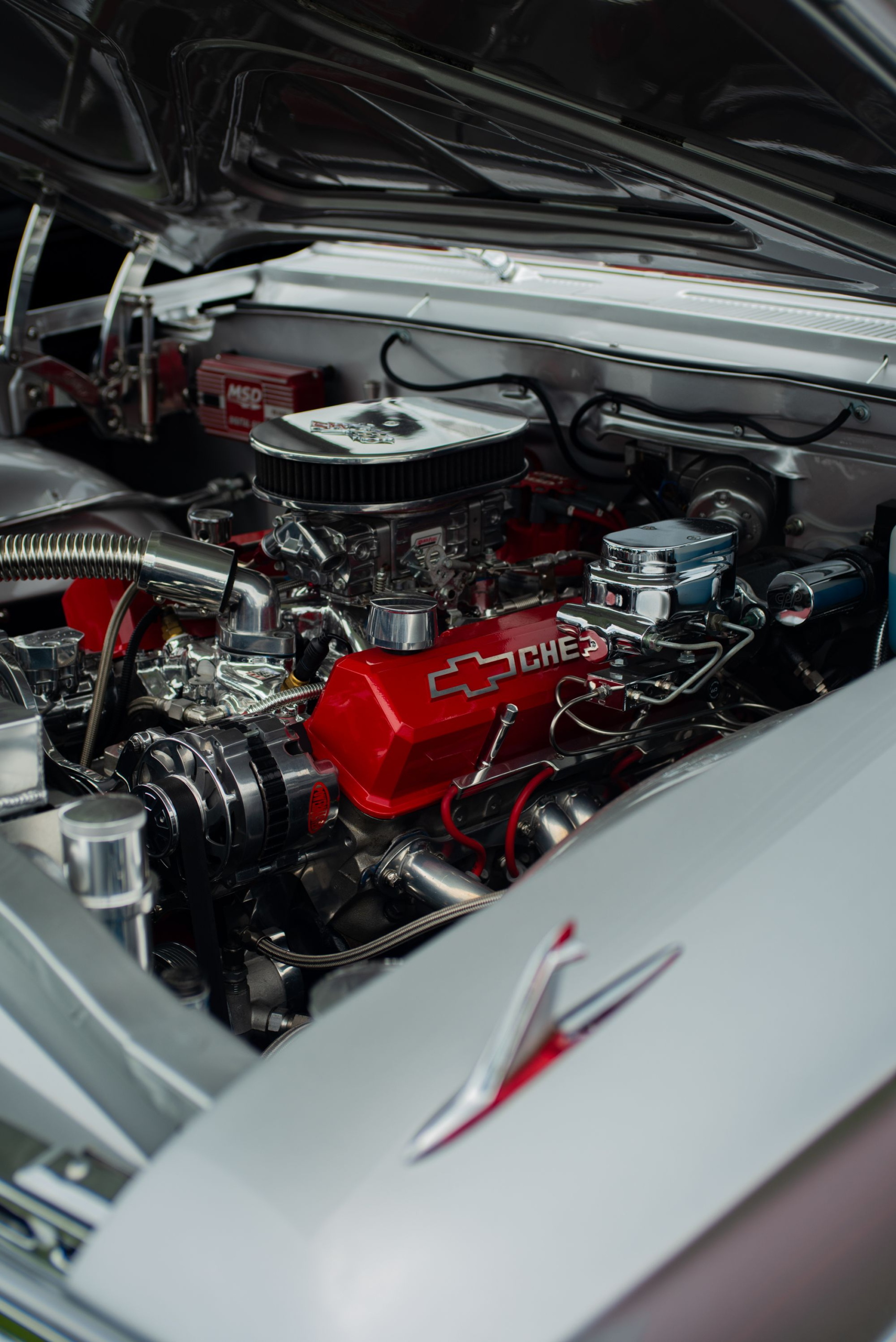 Close-up of a restored Chevrolet V8 engine bay with carburetor, distributor, ignition wiring, and timing components