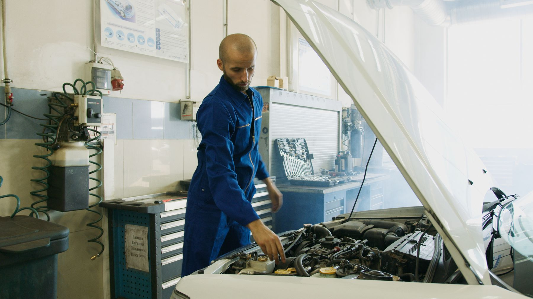 A mechanic looking over an open engine bay in a garage