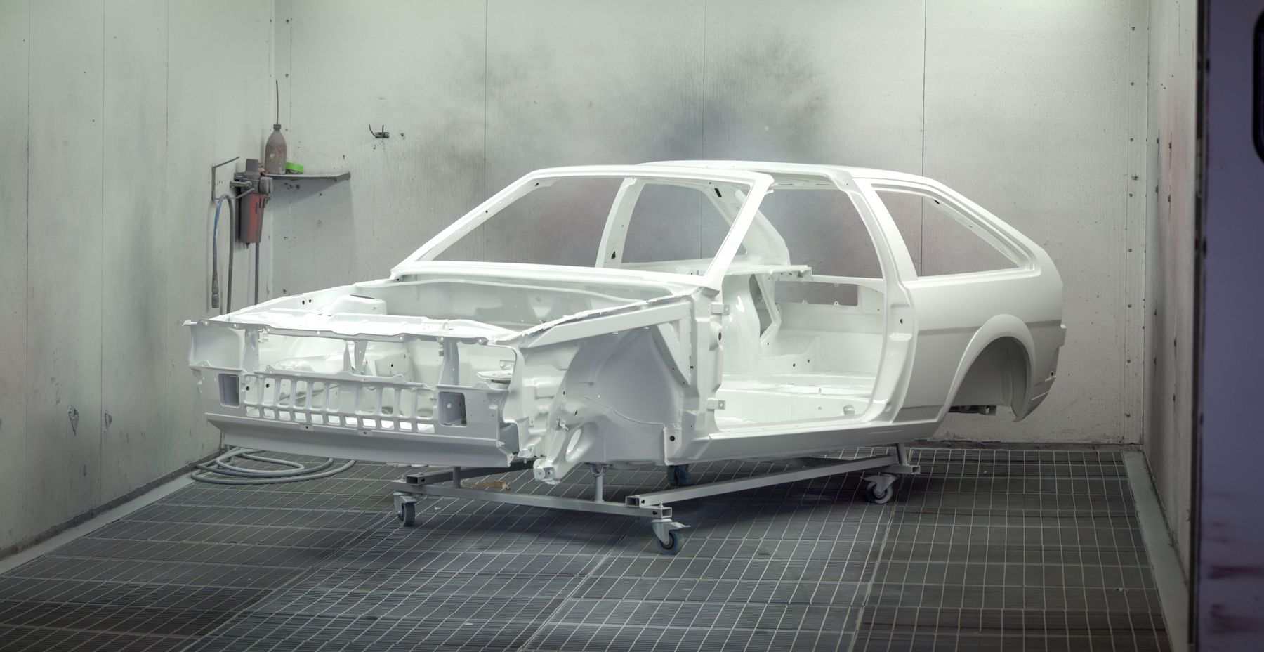 A stripped car body in white primer inside an automotive paint booth