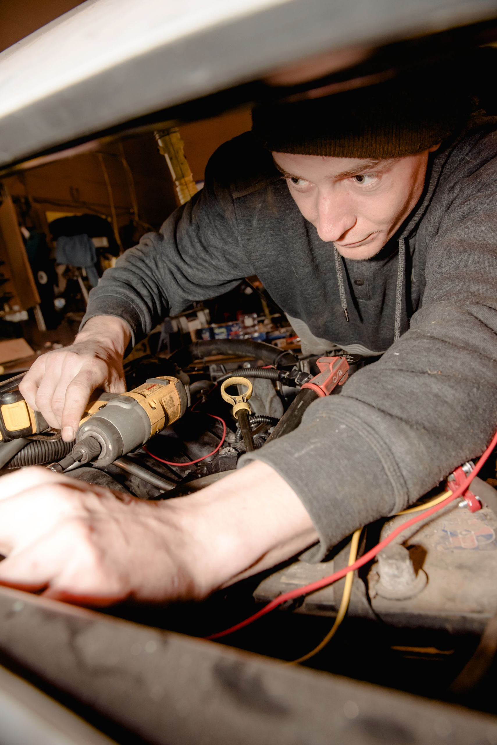 A mechanic repairing a car engine with hand tools in a garage