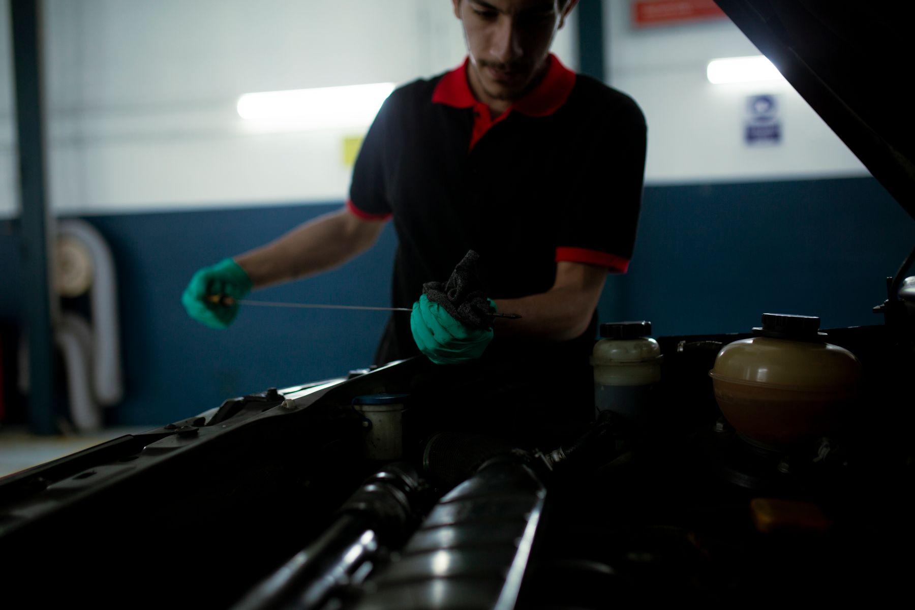 A technician checking engine oil with a dipstick under an open hood