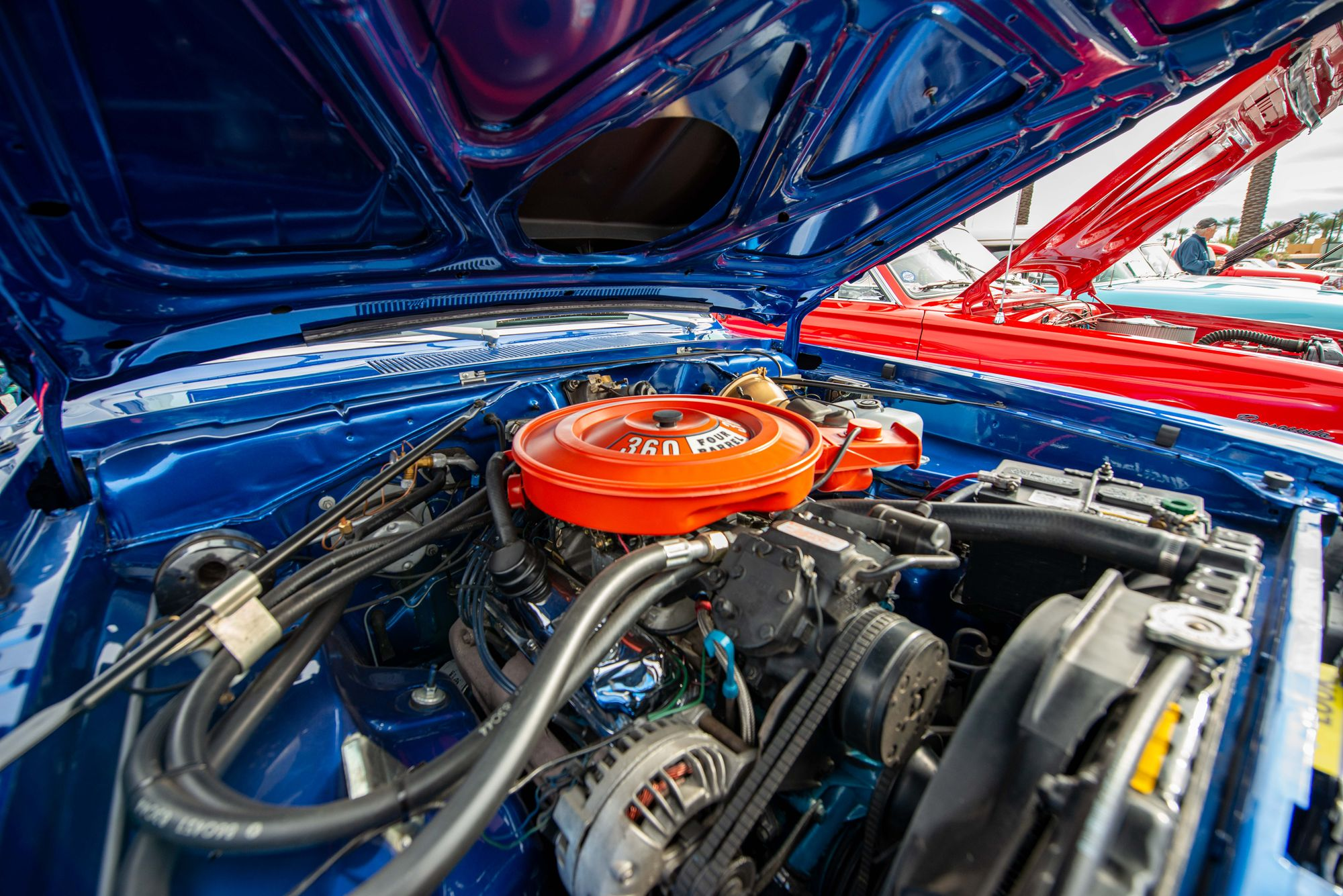 Classic blue muscle car engine bay with orange air cleaner, battery, and alternator visible on a V8