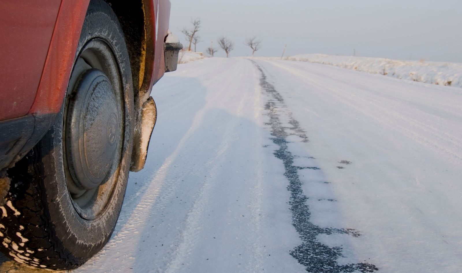 Close-up of a car's front tire rolling on a snow-covered rural road with tire tracks ahead