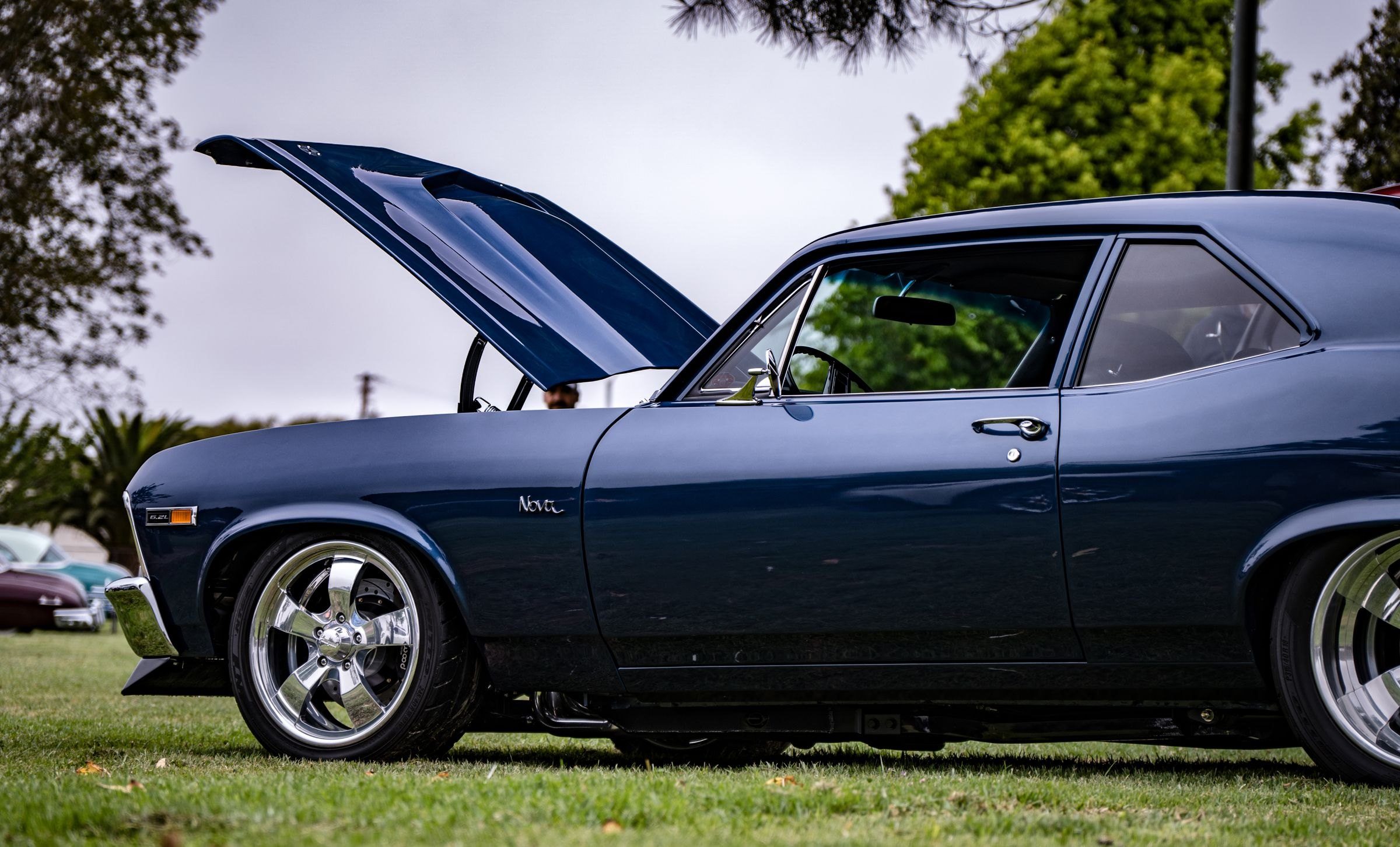 Dark blue Chevrolet Nova with the hood open, parked on grass at an outdoor car show
