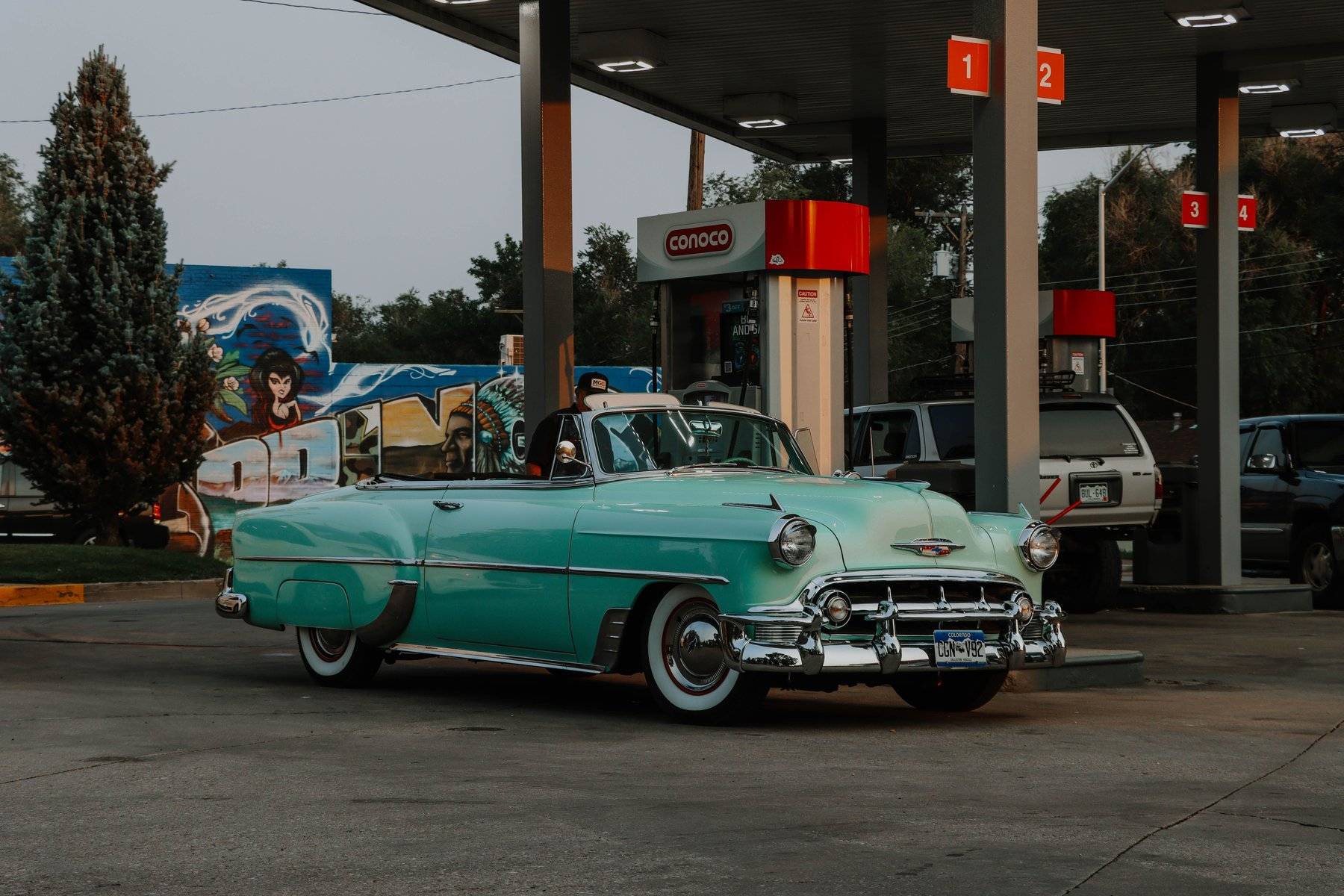Teal early-1950s Chevrolet convertible with whitewall tires parked at a Conoco gas station pump